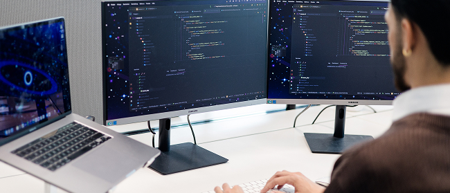 Person sitzt mit dem Rücken zur Kamera vor einem Bildschirm mit Code