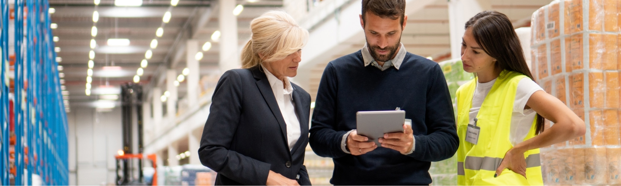 Thre persons in a warehouse looking onto a tablet 