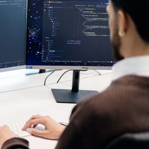 Person sitzt mit dem Rücken zur Kamera vor einem Bildschirm mit Code